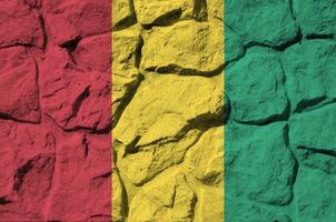 Guinea bandera representado en pintar colores en antiguo Roca pared de cerca. texturizado bandera en rock pared antecedentes foto