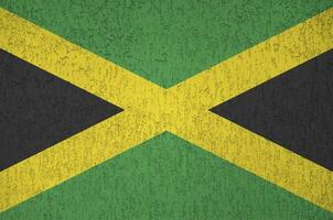 Jamaica flag depicted in bright paint colors on old relief plastering wall. Textured banner on rough background photo