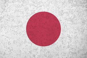 Japan flag depicted in bright paint colors on old relief plastering wall. Textured banner on rough background photo