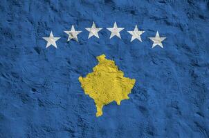 Kosovo flag depicted in bright paint colors on old relief plastering wall. Textured banner on rough background photo