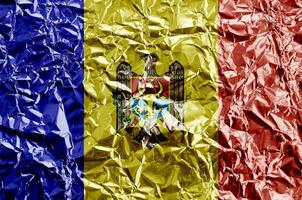 Moldova flag depicted in paint colors on shiny crumpled aluminium foil closeup. Textured banner on rough background photo