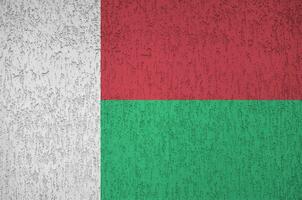Madagascar flag depicted in bright paint colors on old relief plastering wall. Textured banner on rough background photo