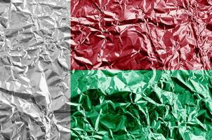 Madagascar flag depicted in paint colors on shiny crumpled aluminium foil closeup. Textured banner on rough background photo