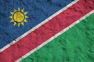 Namibia flag depicted in bright paint colors on old relief plastering wall. Textured banner on rough background photo