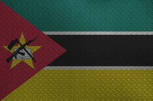 Mozambique flag depicted in paint colors on old brushed metal plate or wall closeup. Textured banner on rough background photo