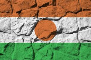 Niger flag depicted in paint colors on old stone wall closeup. Textured banner on rock wall background photo