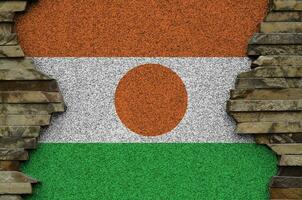 Niger flag depicted in paint colors on old stone wall closeup. Textured banner on rock wall background photo