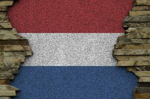 Netherlands flag depicted in paint colors on old stone wall closeup. Textured banner on rock wall background photo