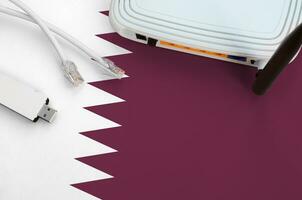 Qatar flag depicted on table with internet rj45 cable, wireless usb wifi adapter and router. Internet connection concept photo
