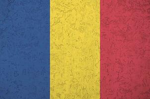 Romania flag depicted in bright paint colors on old relief plastering wall. Textured banner on rough background photo