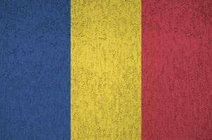 Romania flag depicted in bright paint colors on old relief plastering wall. Textured banner on rough background photo