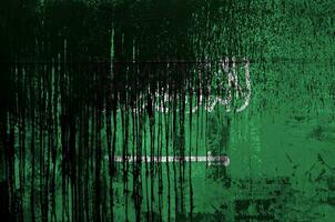 Saudi Arabia flag depicted in paint colors on old and dirty oil barrel wall closeup. Textured banner on rough background photo