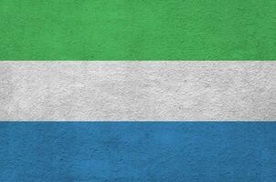 Sierra Leone flag depicted in bright paint colors on old relief plastering wall. Textured banner on rough background photo