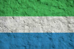 Sierra Leone flag depicted in bright paint colors on old relief plastering wall. Textured banner on rough background photo