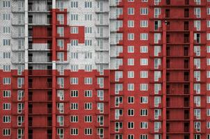 Tonga flag depicted in paint colors on multi-storey residental building under construction. Textured banner on brick wall background photo