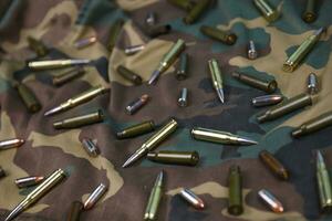 Many rifle bullets and cartridges on dark camouflage background photo