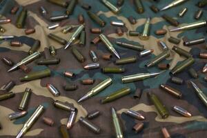 Many rifle bullets and cartridges on dark camouflage background photo