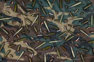 Many rifle bullets and cartridges on dark camouflage background photo