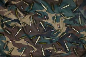 Many rifle bullets and cartridges on dark camouflage background photo