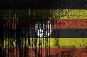 Uganda flag depicted in paint colors on old and dirty oil barrel wall closeup. Textured banner on rough background photo