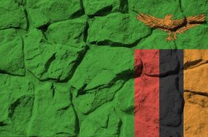 Zambia flag depicted in paint colors on old stone wall closeup. Textured banner on rock wall background photo