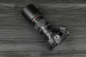 Canon EOS R photocamera and mount adapter EF - EOS R with Canon 105mm f2.8 lens on black wooden table. Photography equipment by Canon inc. photo