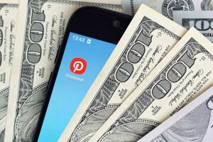 Smartphone screen with Pinterest app and lot of hundred dollar bills. Business and social networking concept photo