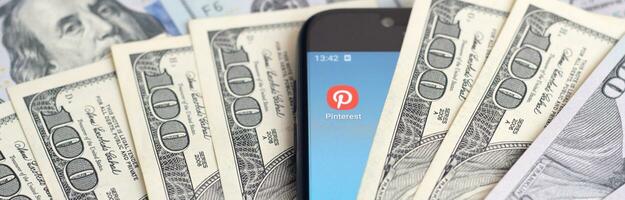 Smartphone screen with Pinterest app and lot of hundred dollar bills. Business and social networking concept photo