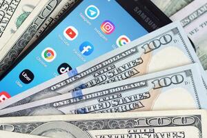 Smartphone screen with many popular apps and lot of hundred dollar bills. Business and social networking concept photo