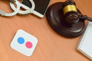 Flickr paper logo lies with wooden judge gavel, smartphone and handcuffs. Entertainment lawsuit concept photo