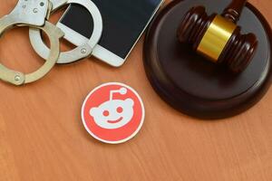 Reddit paper logo lies with wooden judge gavel, smartphone and handcuffs. Entertainment lawsuit concept photo