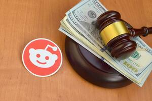 Reddit paper logo lies with judge gavel and hundred dollar bills. Entertainment lawsuit concept photo