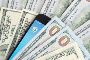 Smartphone screen with Google app and lot of hundred dollar bills. Business and social networking concept photo