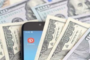 Smartphone screen with Pinterest app and lot of hundred dollar bills. Business and social networking concept photo