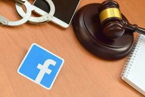 Facebook paper logo lies with wooden judge gavel, smartphone and handcuffs. Entertainment lawsuit concept photo