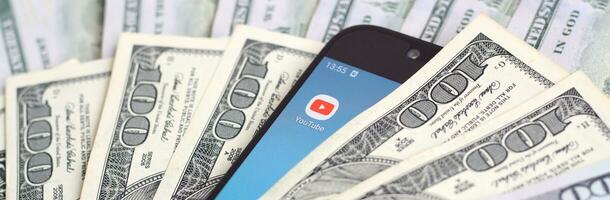 Smartphone screen with Youtube app and lot of hundred dollar bills. Business and social networking concept photo