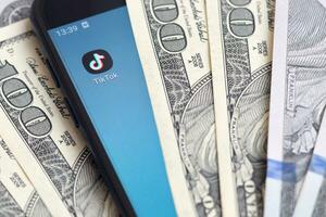 Smartphone screen with Tiktok app and lot of hundred dollar bills. Business and social networking concept photo