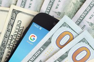 Smartphone screen with Google app and lot of hundred dollar bills. Business and social networking concept photo