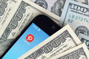 Smartphone screen with Pinterest app and lot of hundred dollar bills. Business and social networking concept photo