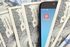Smartphone screen with Pinterest app and lot of hundred dollar bills. Business and social networking concept photo