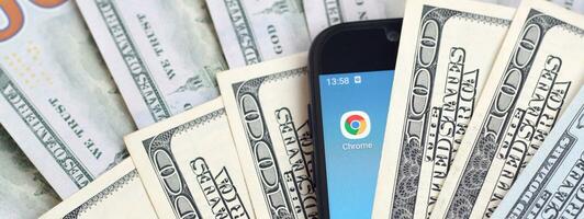 pantalla de teléfono inteligente con la aplicación google chrome y muchos billetes de cien dólares. concepto de negocios y redes sociales foto