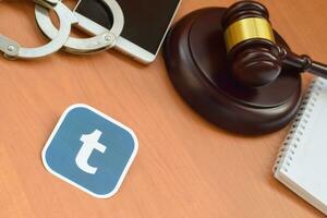 Tumblr paper logo lies with wooden judge gavel, smartphone and handcuffs. Entertainment lawsuit concept photo