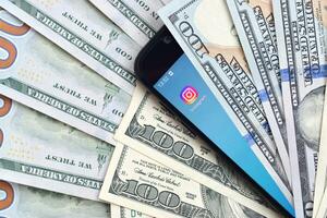 Smartphone screen with Instagram app and lot of hundred dollar bills. Business and social networking concept photo