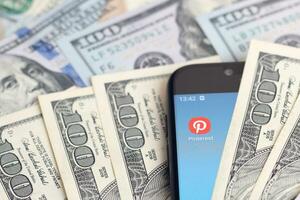Smartphone screen with Pinterest app and lot of hundred dollar bills. Business and social networking concept photo