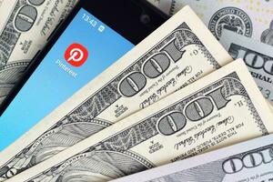 Smartphone screen with Pinterest app and lot of hundred dollar bills. Business and social networking concept photo