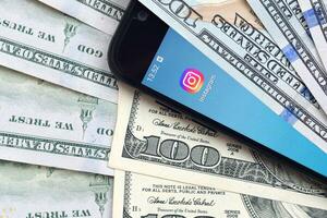 Smartphone screen with Instagram app and lot of hundred dollar bills. Business and social networking concept photo