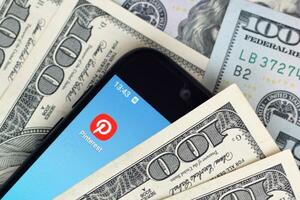 Smartphone screen with Pinterest app and lot of hundred dollar bills. Business and social networking concept photo