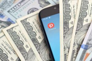 Smartphone screen with Pinterest app and lot of hundred dollar bills. Business and social networking concept photo