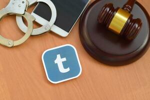 Tumblr paper logo lies with wooden judge gavel, smartphone and handcuffs. Entertainment lawsuit concept photo