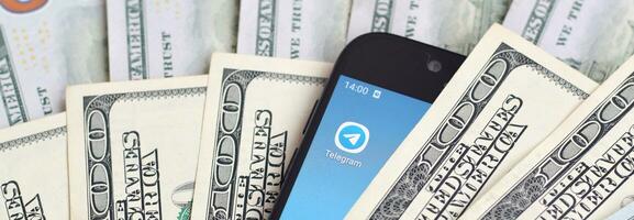 Smartphone screen with Telegram app and lot of hundred dollar bills. Business and social networking concept photo